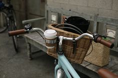 a bicycle parked next to a bench with a basket full of coffee cups on it