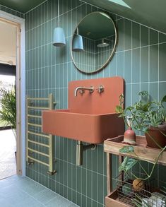 a sink and mirror in a room with green tiles on the wall, potted plants next to it