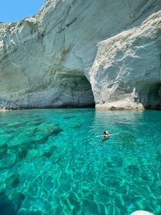 a person swimming in clear blue water next to a large white rock formation and cliffs