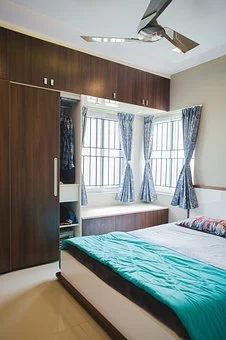 a bed sitting under a window next to a wooden dresser and closet in a bedroom