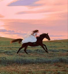 a woman riding on the back of a brown horse across a lush green grass covered field