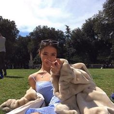 a woman in a blue dress is sitting on the grass with a blanket over her