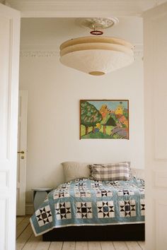 a bed sitting under a painting next to a white door in a room with wooden floors