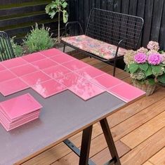 a table with pink tiles on it and some flowers in the back ground next to a bench