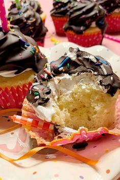 A yellow birthday party cupcake topped with meringue and a chocolate shell with sprinkles.