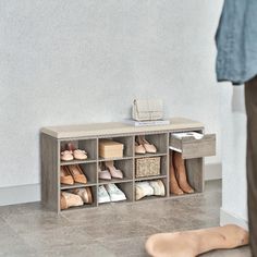 a wooden shoe rack with several pairs of shoes on it next to a person's foot