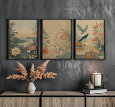 three paintings hang on the wall next to a vase with flowers and candles in it