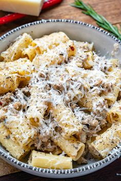 a bowl filled with pasta and meat covered in parmesan cheese on top of a wooden table