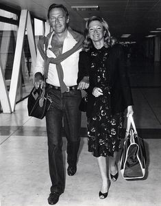 a man and woman walking through an airport holding hands with each other while carrying bags