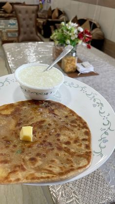 a pancake on a plate with a bowl of butter next to it and some flowers in the background