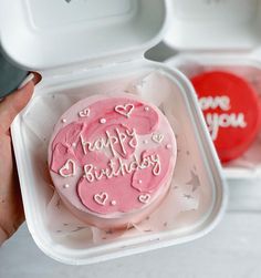 a pink frosted birthday cake in a plastic container