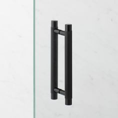 a black handle on a glass door with white marble walls in the backround