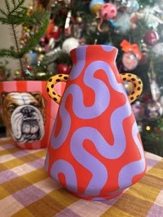 a red and purple vase sitting on top of a table next to a christmas tree