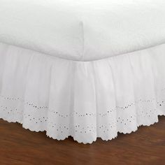 a bed with white bedspread on top of it and wood flooring underneath