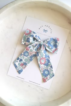 a blue and pink flowered bow sitting on top of a white plate next to a card