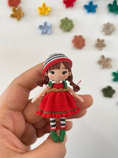 a hand holding a tiny doll made from crochet yarns and beads, in front of many small flowers