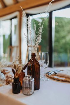 the table is set with two vases and three empty wine glasses, one has dried grass in it