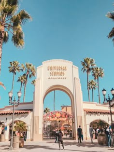 the entrance to universal studios with palm trees in the foreground and people walking around