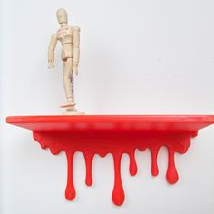 a wooden mannequin standing on top of a red shelf with blood dripping down it