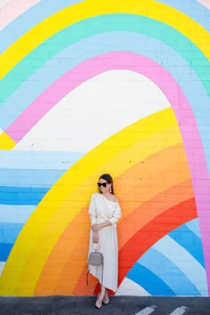 a woman standing in front of a colorful wall with her hand on her hip while wearing sunglasses