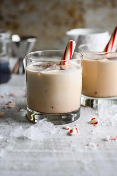 two glasses filled with candy canes on top of a white table cloth covered in snow