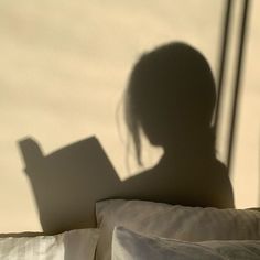 the shadow of a person reading a book on a bed