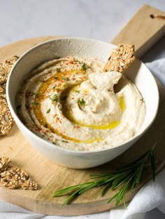 a white bowl filled with hummus and crackers on top of a cutting board