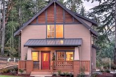 a small house in the woods with a porch and covered front door is lit up at night