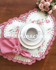 there is a cup and saucer on the table with pink roses around it,