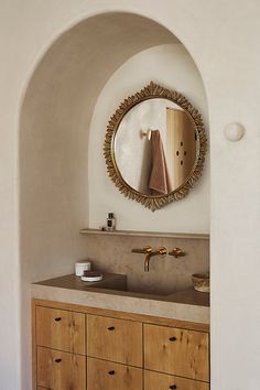 a bathroom vanity with two sinks under a round mirror and gold faucet on the wall