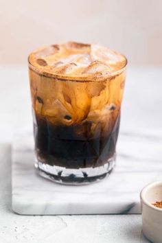 an iced drink in a glass on top of a marble counter next to a white bowl