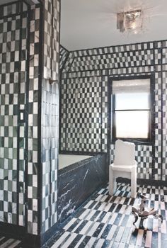 a bathroom with black and white tiles on the walls, flooring and a chair