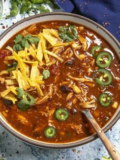 a bowl of chili and cheese soup with a wooden spoon