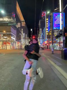 two people are hugging on the street at night