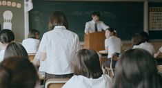 a group of children sitting at desks in front of a blackboard with an instructor