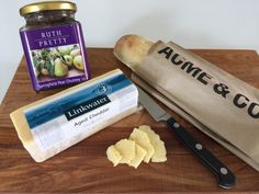 an assortment of food on a cutting board including bread, butter, jam and crackers