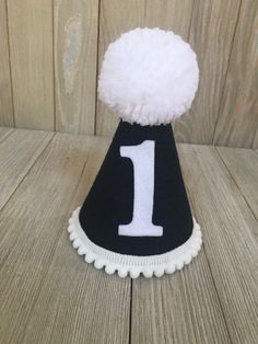 Please read shop announcement for current processing times and updates. Your birthday boy will look absolutely adorable in this mini birthday hat for his half birthday or whole birthday! Perfect for a party or photo shoot. This hat is available as a mini size (5 inches tall by 4 inches wide) Or a full size (7 inches tall by 5 inches wide). It features black felt with a white number of your choice. White mini pom pom ribbon is attached along the base of the hat with a yarn Pom Pom on top. It has Black And White Birthday, First Birthday Hat, 1st Birthday Hats, First Birthday Hats, Mini Pom, Mini Hats, Half Birthday, Yarn Pom Pom, White Birthday