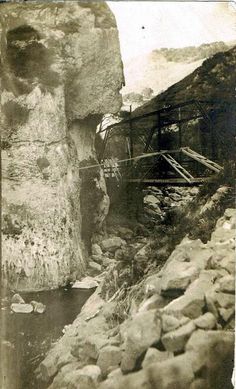 an old black and white photo of a bridge over a river with rocks on both sides