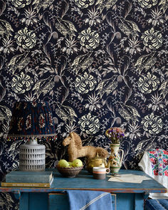 a blue table topped with fruit next to a wallpaper covered in flowers and leaves