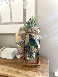 a wooden table topped with a vase filled with greenery and a bow on top of it