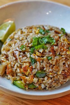 a white bowl filled with rice and vegetables on top of a wooden table next to a slice of lime