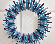 a circular mirror made out of strips of colored wood and plastic tubes, hanging on the wall