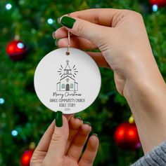 a person holding up a christmas ornament in front of a tree with lights