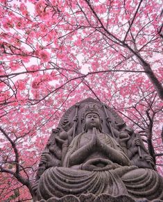 there is a statue in the middle of some trees with pink flowers on it's branches