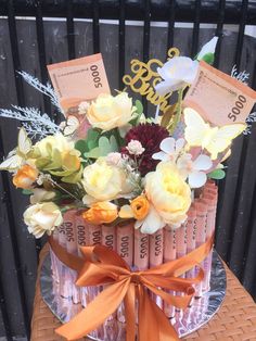 an arrangement of flowers and money are on top of a glass plate with orange ribbon