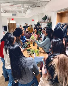 a group of people sitting around a wooden table with plants in the middle of it