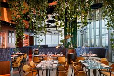 a restaurant with tables, chairs and plants hanging from the ceiling in front of large windows