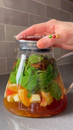 a person is holding a spoon over a jar filled with fruit and minty tea