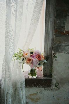 a bouquet of flowers sitting on top of a window sill next to a curtain