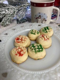 four cookies on a white plate next to a coffee cup and christmas tree in the background